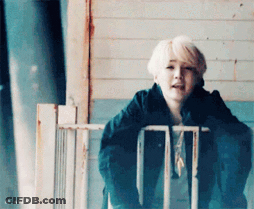 Blonde Young Man Standing Next To Fence Looking At Camera GIF
