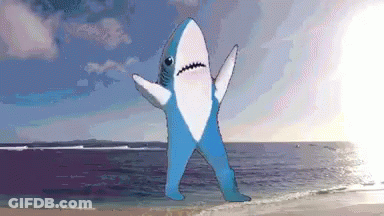 Blue And White Shark Standing On Beach With Arms Outstretched GIF