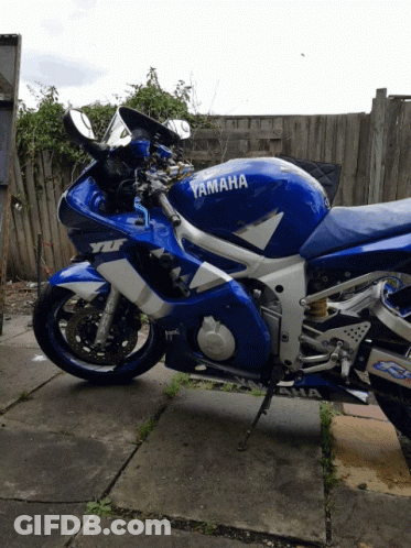 Blue And White Yamaha Motorcycle Parked In Front Of Fence GIF