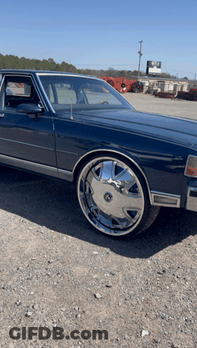 Blue Car With Chrome Wheels Parked On Gravel GIF