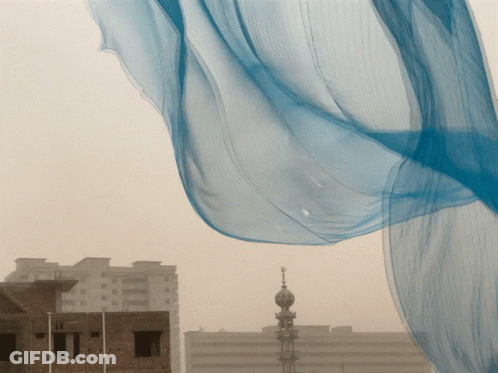 Blue Cloth Blowing In Wind In Front Of Brick Building GIF