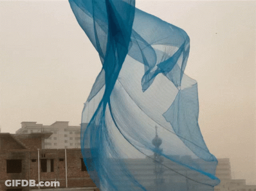 Blue Cloth Blowing In Wind In Front Of City GIF