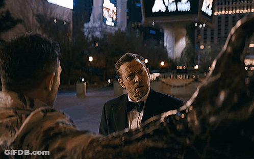 Blurry Man In Tuxedo Walking Past Sign Saying A GIF