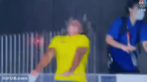 Blurry Man In Yellow Shirt Next To Fence GIF