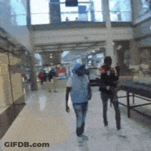 Blurry Picture Of People Walking In Mall With Sign Saying A GIF