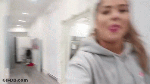 Blurry Woman In Gray Hoodie Standing In Hallway GIF