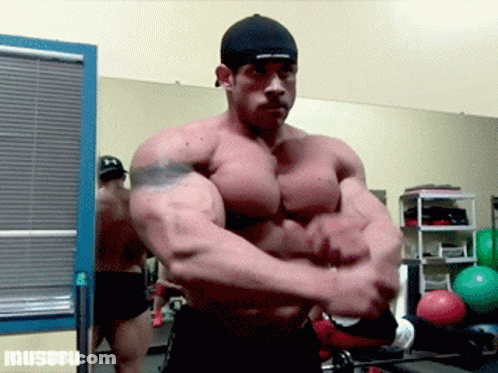 Bodybuilder Flexing Muscles In Front Of Muscul Sign GIF