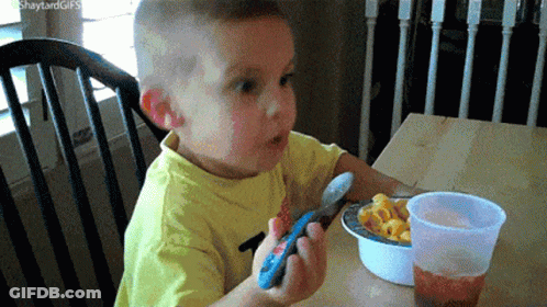 Boy Eating Macaroni And Cheese Holding Remote GIF