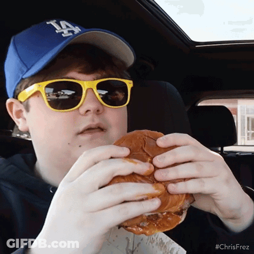 Boy In LA Hat And Sunglasses Eating Hamburger GIF