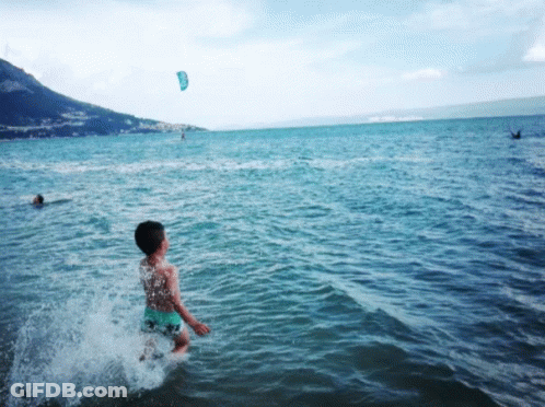 Boy Splashing In Ocean With Kite GIF