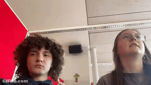 Boy With Curly Hair And Girl With Glasses Standing By Cross GIF