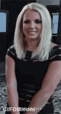 Britney Spears Is Wearing A Black Dress And Smiling While Standing With Her Hands Behind Her Back . GIF