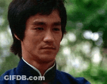 Bruce Lee Is Wearing A Blue Jacket And Looking At The Camera With A Serious Look On His Face . GIF