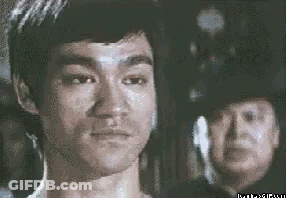 Bruce Lee Looking At Camera, Man In Police Hat Behind GIF