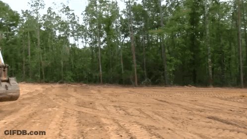 Bulldozer Driving Through Dirt Field In Woods GIF