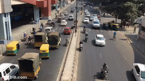 Busy Street With Cars And Motorcycles And Sign Saying A GIF