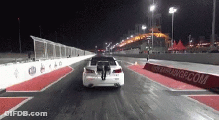 Car Driving Down Race Track At Night With Person Standing On Back GIF