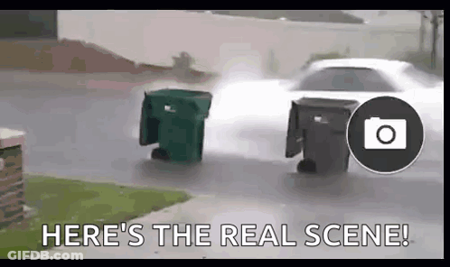 Car Driving Down Street Next To Two Garbage Cans In Rain GIF