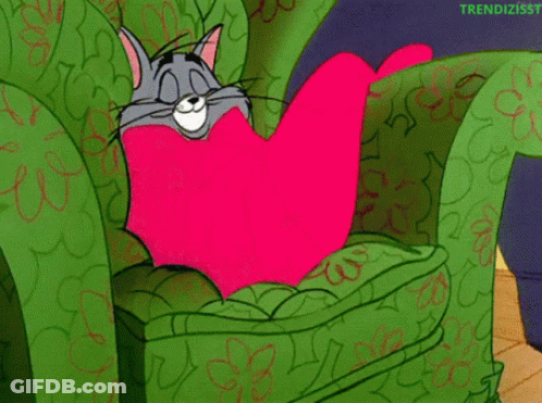 Cartoon Cat Sitting In Green Chair With Pink Heart Pillow GIF