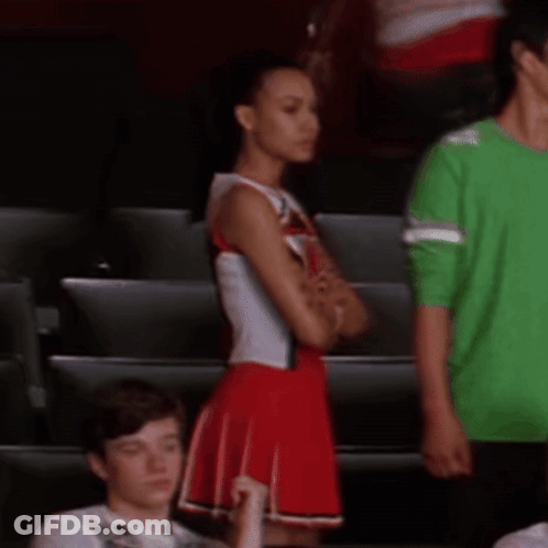 Cheerleader In Red And White Uniform Next To Man In Green Shirt GIF