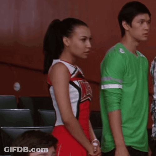 Cheerleader In Red And White Uniform With WMHS Beside Man In Green Shirt GIF