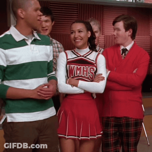 Cheerleader In WMHS Uniform Smiling Beside Man In Green And White Striped Shirt GIF