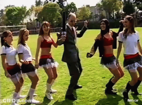 Cheerleaders Dancing On Field With Suited Man Holding Gun GIF