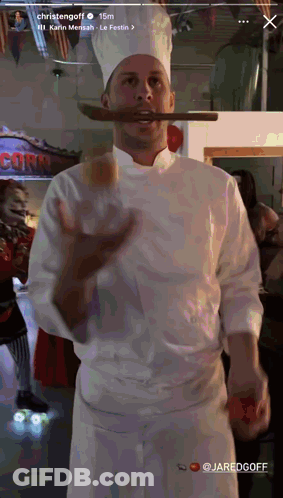 Chef Holding Sausage In Mouth In Front Of Corn Sign GIF