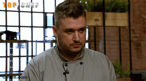 Chef In Uniform In Front Of Top Chef Screen GIF