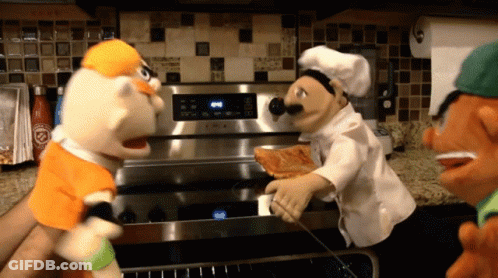 Chef Puppet Holding Pizza In Front Of Stove GIF