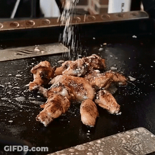 Chicken Wings Are Being Sprinkled With Salt On A Griddle GIF