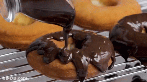 Chocolate Icing Is Being Poured On A Donut On A Rack . GIF