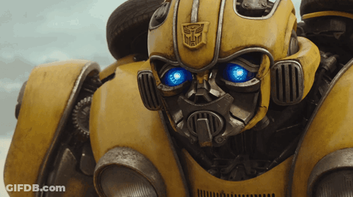 Close Up Yellow Robot With Blue Eyes And Transformer Logo GIF