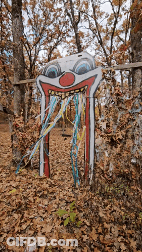 Clown Face Painted On Wooden Sign In Woods GIF