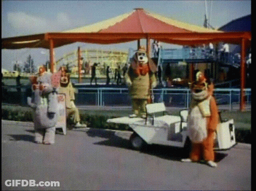 Clowns Standing In Front Of Carousel And Small Car GIF