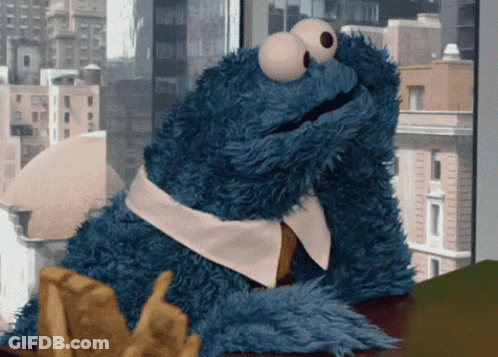 Cookie Monster From Sesame Street Sitting On A Table With A Cookie In His Hand GIF