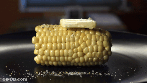 Corn On The Cob With Butter On Top Of It On A Black Plate GIF
