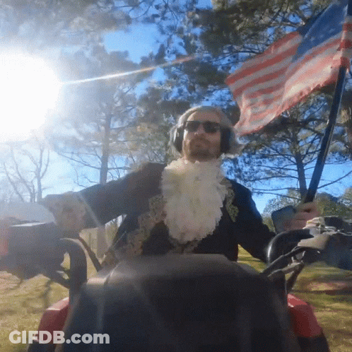 Costumed Man Riding Golf Cart With American Flag GIF