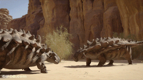 Couple Of Dinosaurs Standing Near Rock Formation GIF