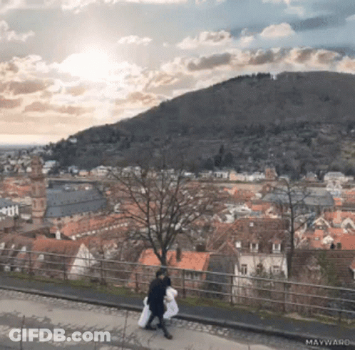 Couple Walking On Sidewalk With Mountain And Maywand GIF