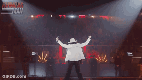 Cowboy Hat Man On Stage With Fireworks And Ultimate Muscleman Sign GIF