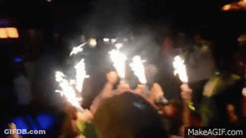 Crowd Holding Sparklers In Dark Room GIF