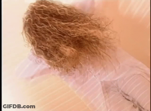 Curly Hair Woman Laying On Bed In White Shirt GIF