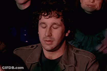Curly Haired Man In Crowd Hand On Chin Eyes Closed GIF