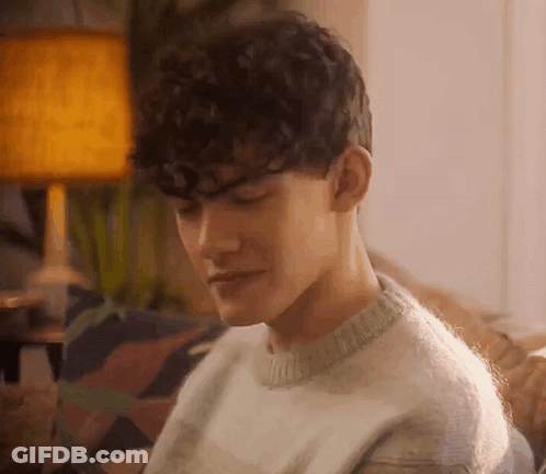 Curly-Haired Man In Sweater On Couch GIF