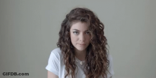 Curly-Haired Woman In White Shirt Looking At Camera GIF
