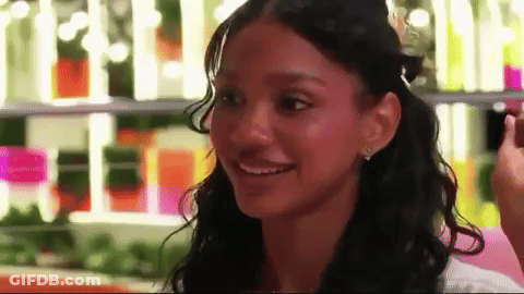 Curly-Haired Woman Smiling At Bottle Shelf GIF