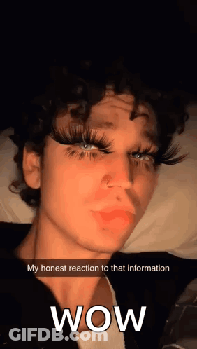 Curly-Haired Young Man With Fake Eyelashes On Bed Says Wow GIF