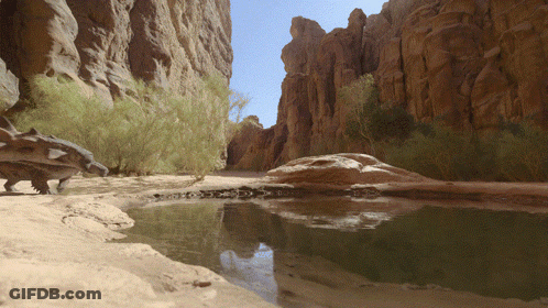 Dinosaur Standing In Sand Near Rock GIF