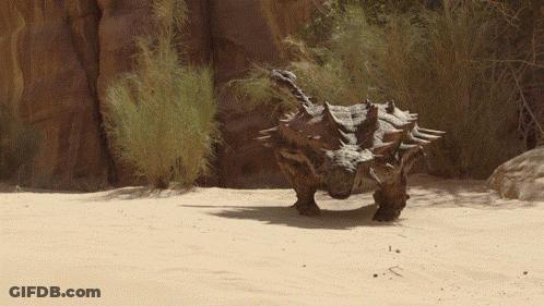 Dinosaur Standing In Sand Near Rock GIF